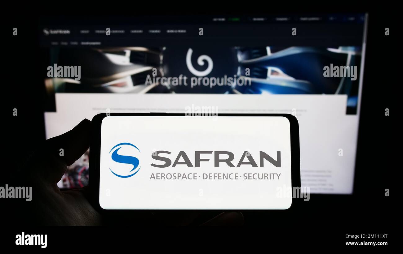 Persona che tiene uno smartphone con il logo della società aerospaziale francese Safran S.A. sullo schermo di fronte al sito Web. Messa a fuoco sul display del telefono. Foto Stock