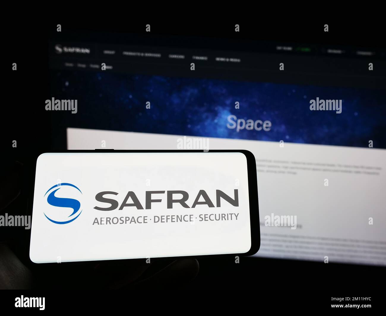 Persona che tiene il telefono cellulare con il logo della società aerospaziale francese Safran SA sullo schermo di fronte alla pagina web aziendale. Messa a fuoco sul display del telefono. Foto Stock