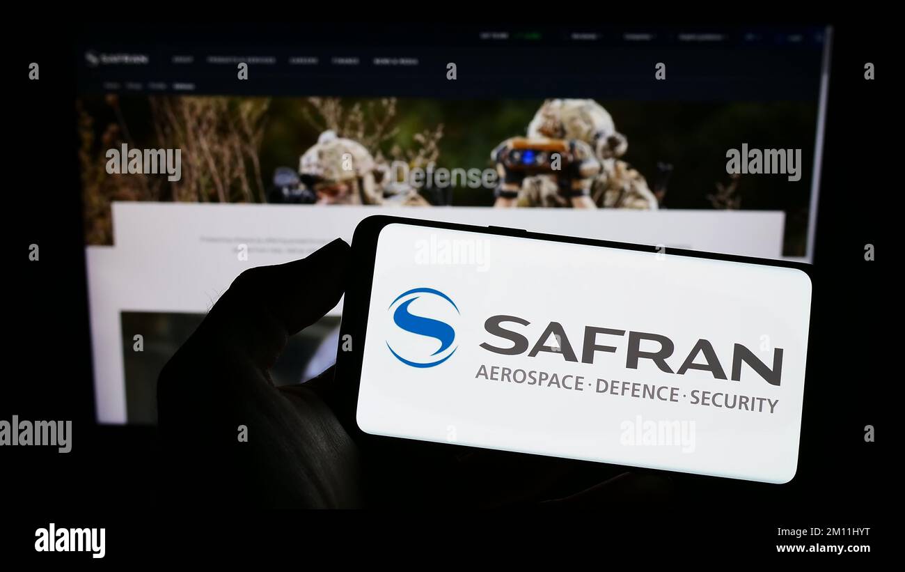 Persona che tiene il cellulare con il logo della società aerospaziale francese Safran S.A. sullo schermo di fronte al sito web aziendale. Messa a fuoco sul display del telefono. Foto Stock