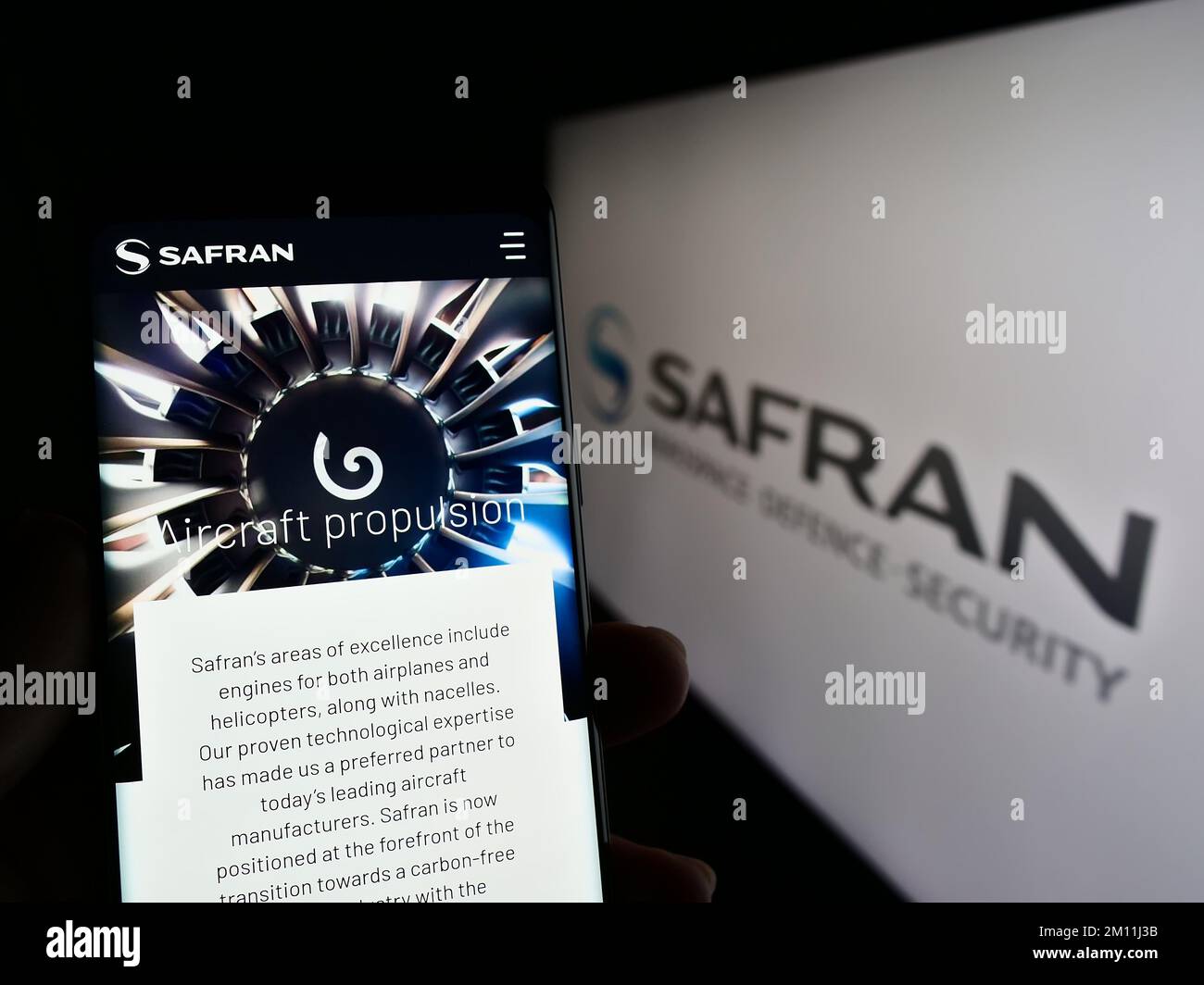 Persona che tiene il telefono cellulare con la pagina web della società aerospaziale francese Safran S.A. sullo schermo di fronte al logo. Messa a fuoco al centro del display del telefono. Foto Stock