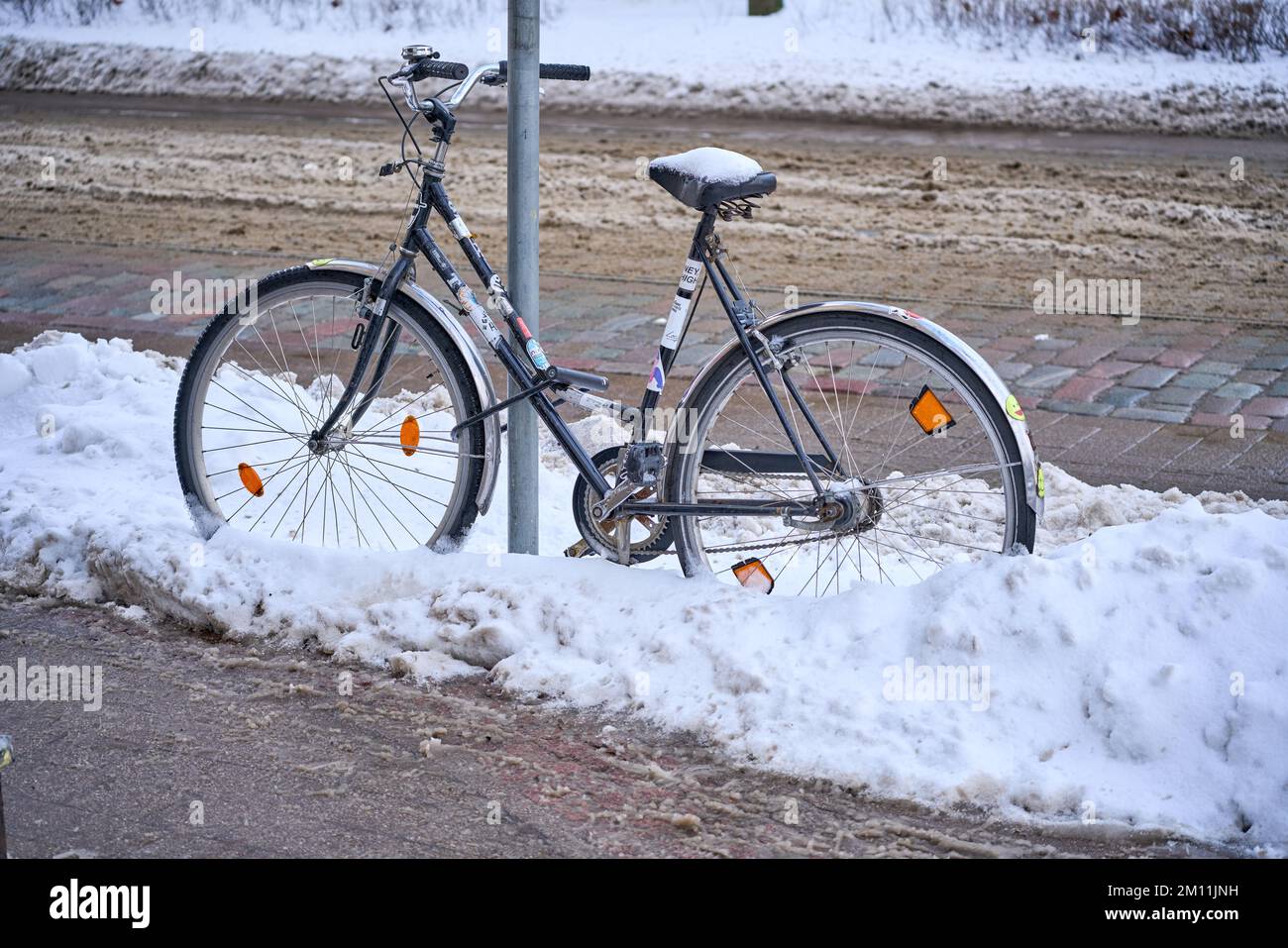 Riga, Lettonia - 8 dicembre, 2022: Bicicletta incatenata ad un palo su una strada cittadina in inverno Foto Stock