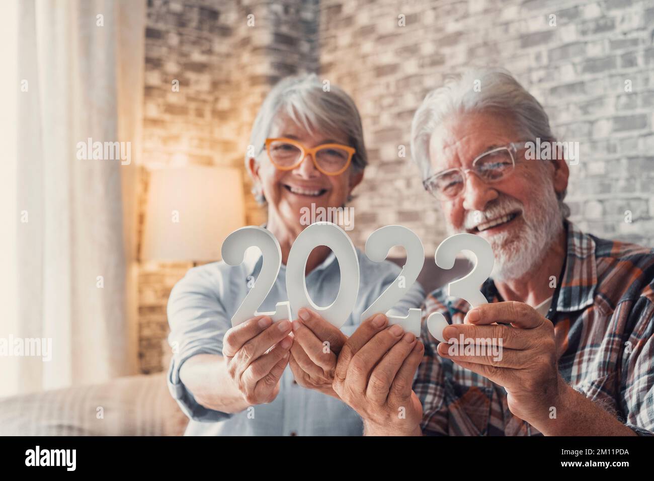 Ritratto di coppia di due anziani pensionati con un numero di 2023 a casa. Primo piano dei numeri di nuovo anno, festeggiamenti e obiettivi per il nuovo concetto di vita. Foto Stock