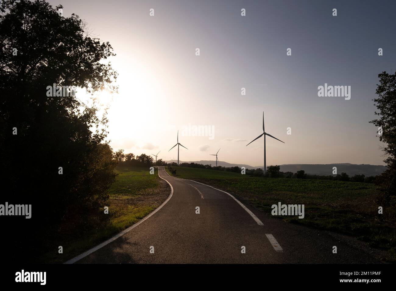 Strada in campi agricoli con turbine eoliche che generano elettricità pulita in Catalogna Spagna Foto Stock