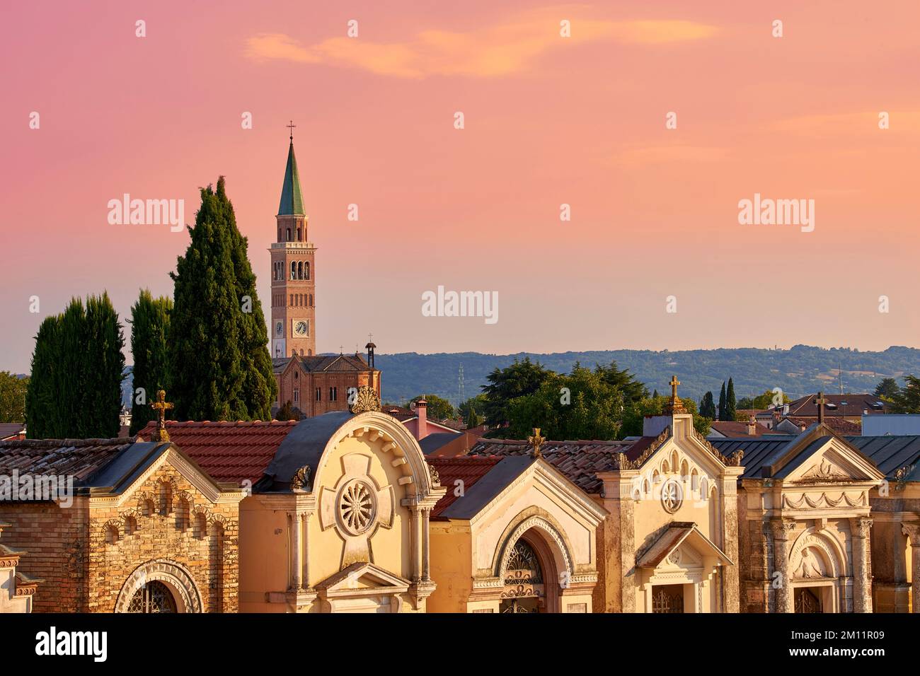 Vista su un cimitero di Pieve di Soligo nella luce dell'ultima sera. Sullo sfondo la torre della chiesa di Parrocchia del Duomo Santa Maria Assunta Foto Stock