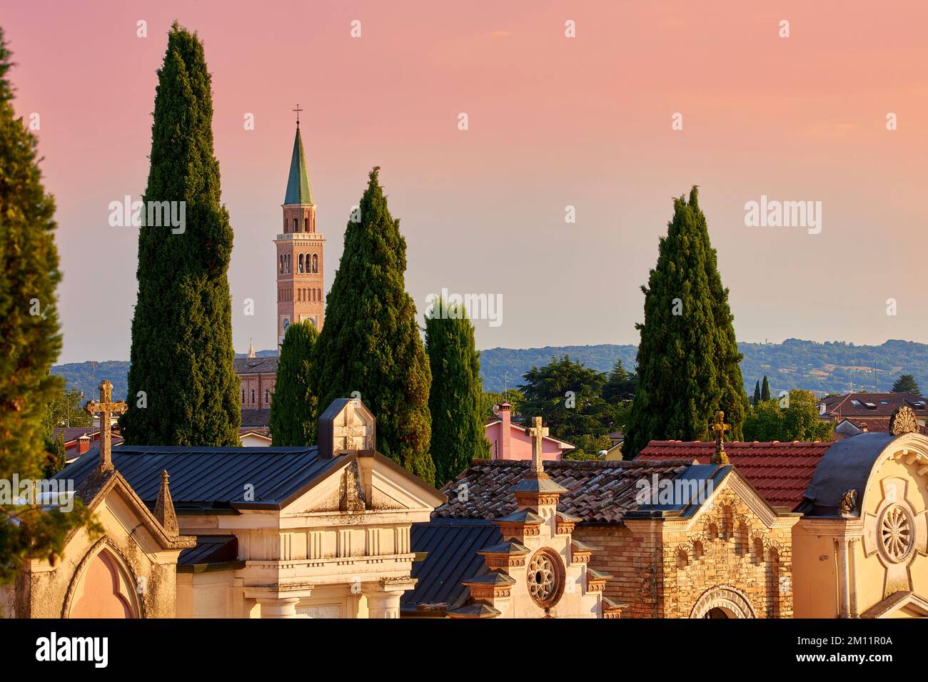 Vista su un cimitero di Pieve di Soligo nella luce dell'ultima sera. Sullo sfondo la torre della chiesa di Parrocchia del Duomo Santa Maria Assunta Foto Stock