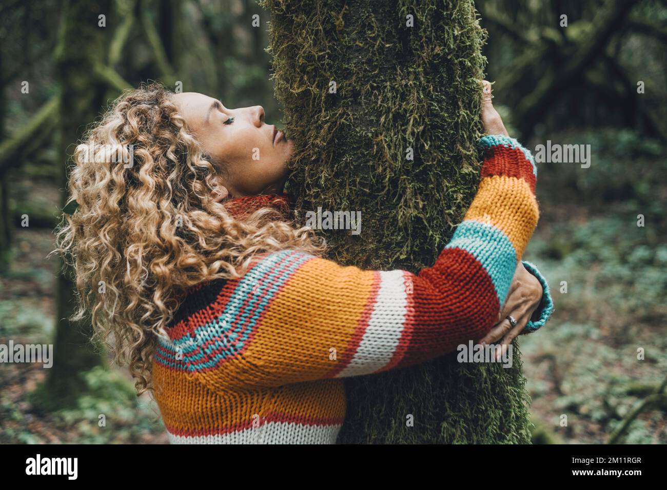 Vista laterale di una donna che abbraccia un albero con muschio verde innamorato. Concetto di persone e ambiente. Attività ricreative all'aperto femminile nei boschi. La protezione della natura contro il cambiamento climatico e il caldo globale Foto Stock
