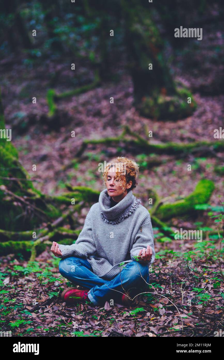 Donna sana lifestyle seduta a terra in posizione di yoga di loto con boschi verdi natura foresta intorno. Donne e zen meditazione attività tempo libero all'aperto. Persone e natura Foto Stock