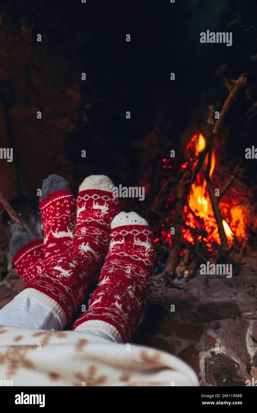 POV di coppia piedi che scalda vicino al camino a casa o nella stanza dello chalet. Vacanze di Natale. La gente romantica gode il rapporto e la tenerezza che osserva il fuoco all'interno. Calze di Natale rosse e bianche Foto Stock