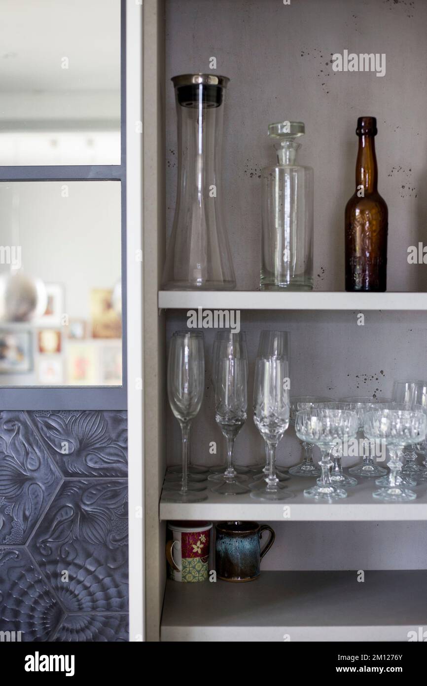 Vista in un armadio da cucina aperto con bicchieri e bottiglie decorati con cura Foto Stock