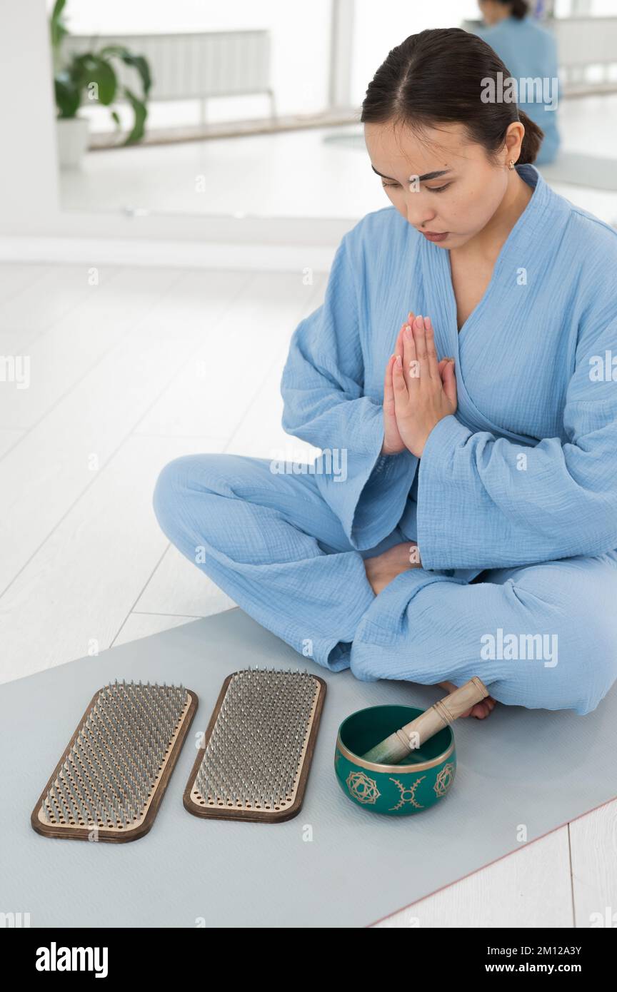 Donna asiatica seduta sul tappeto yoga con ciotola tibetana e tavole sadhu. Foto Stock