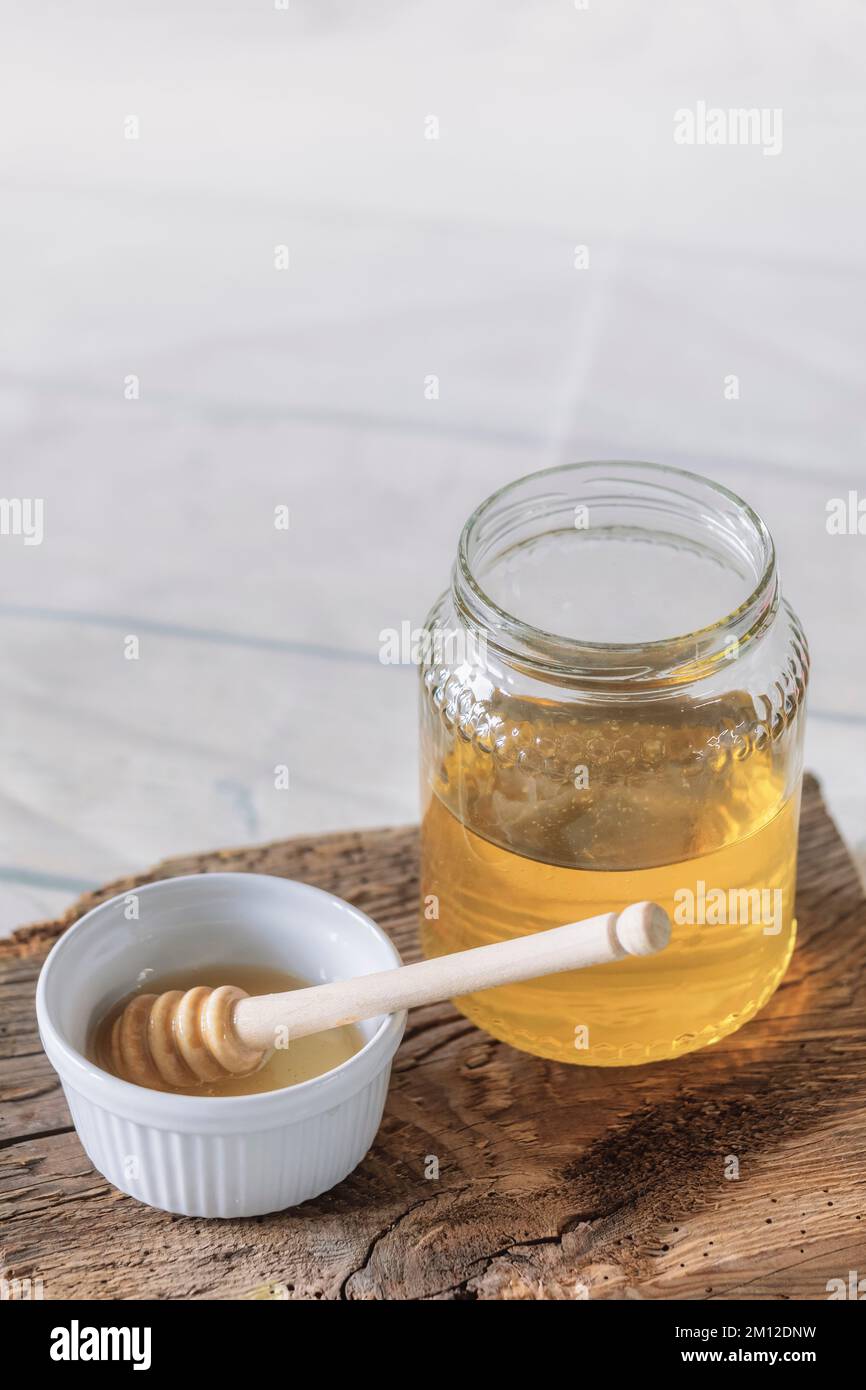 vasetto di vetro di miele d'api con piccola tazza e cucchiaia di miele su antico asse di legno Foto Stock