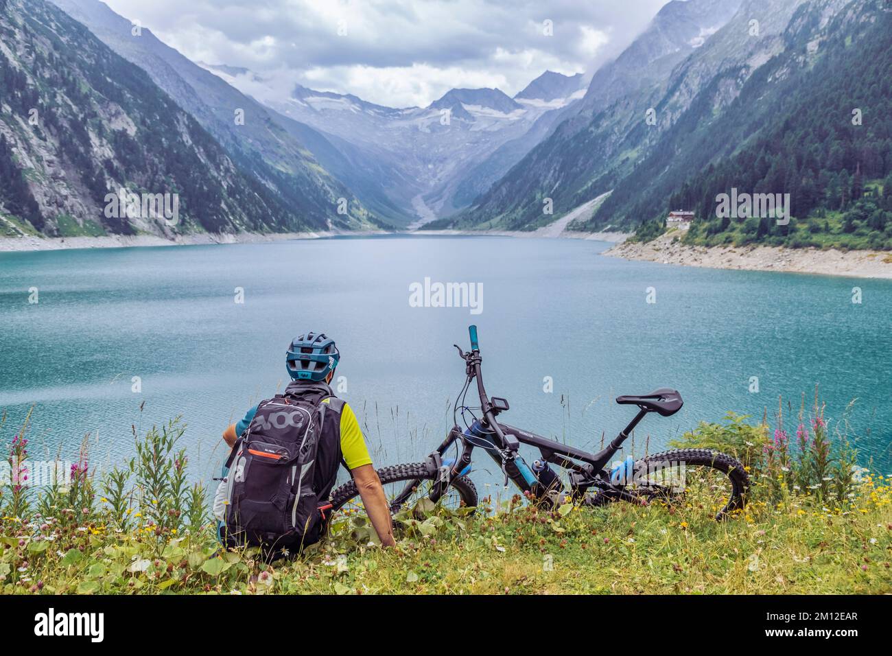 Austria, Tirolo, Zillertal, Finkenberg, ciclista con e-bike seduto sulla riva del lago Schlegeis Stausee Foto Stock