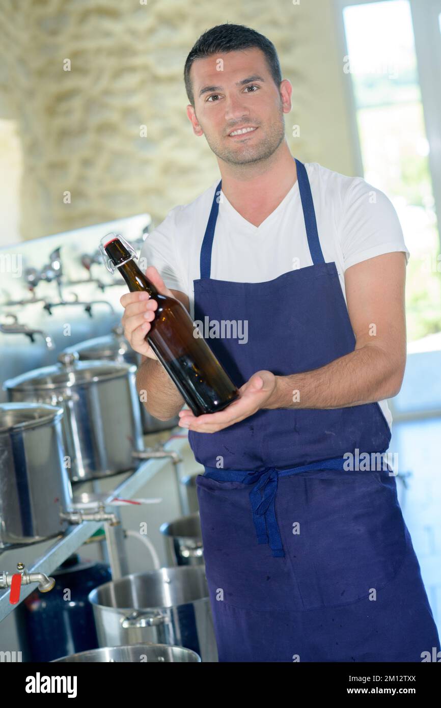 giovane uomo attraente che mostra una birra in bottiglia in fabbrica Foto Stock