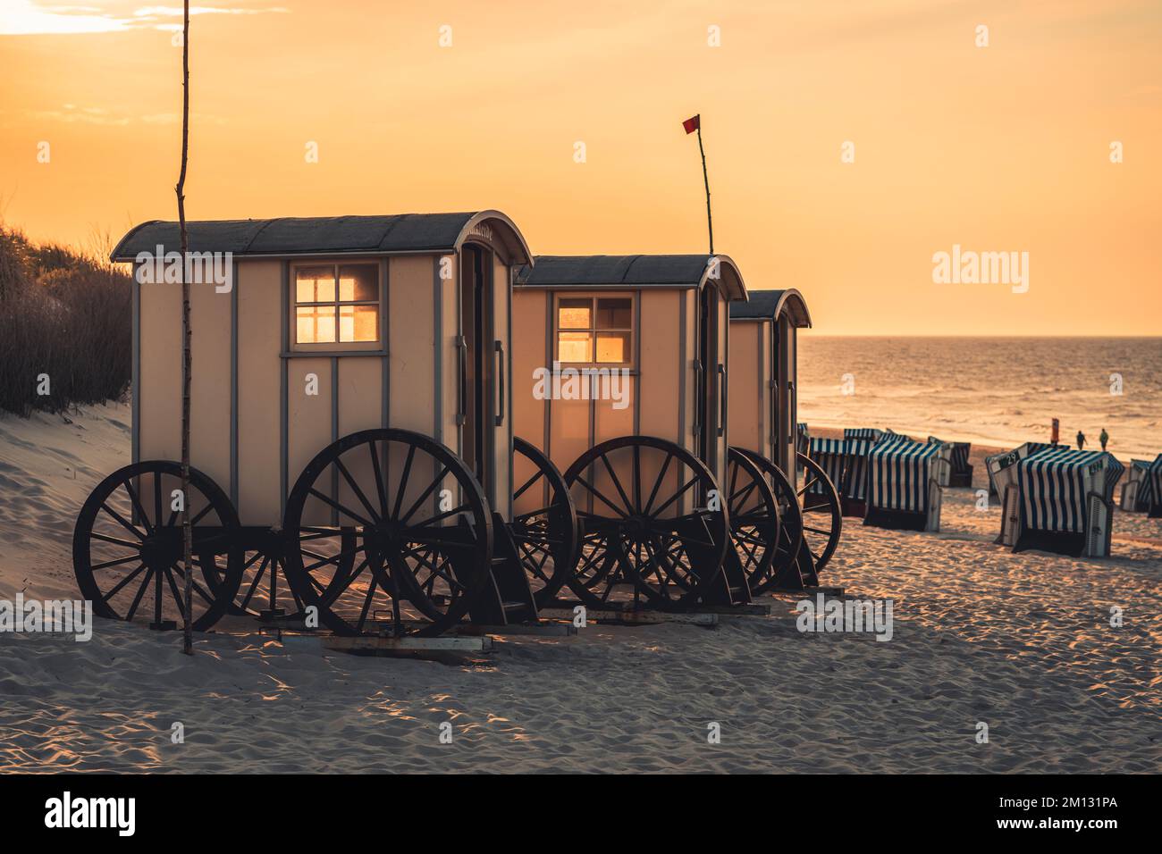 Spogliatoi sulla spiaggia di sera, sedie a sdraio, sullo sfondo il Mare del Nord, persone sfocate in lontananza Foto Stock