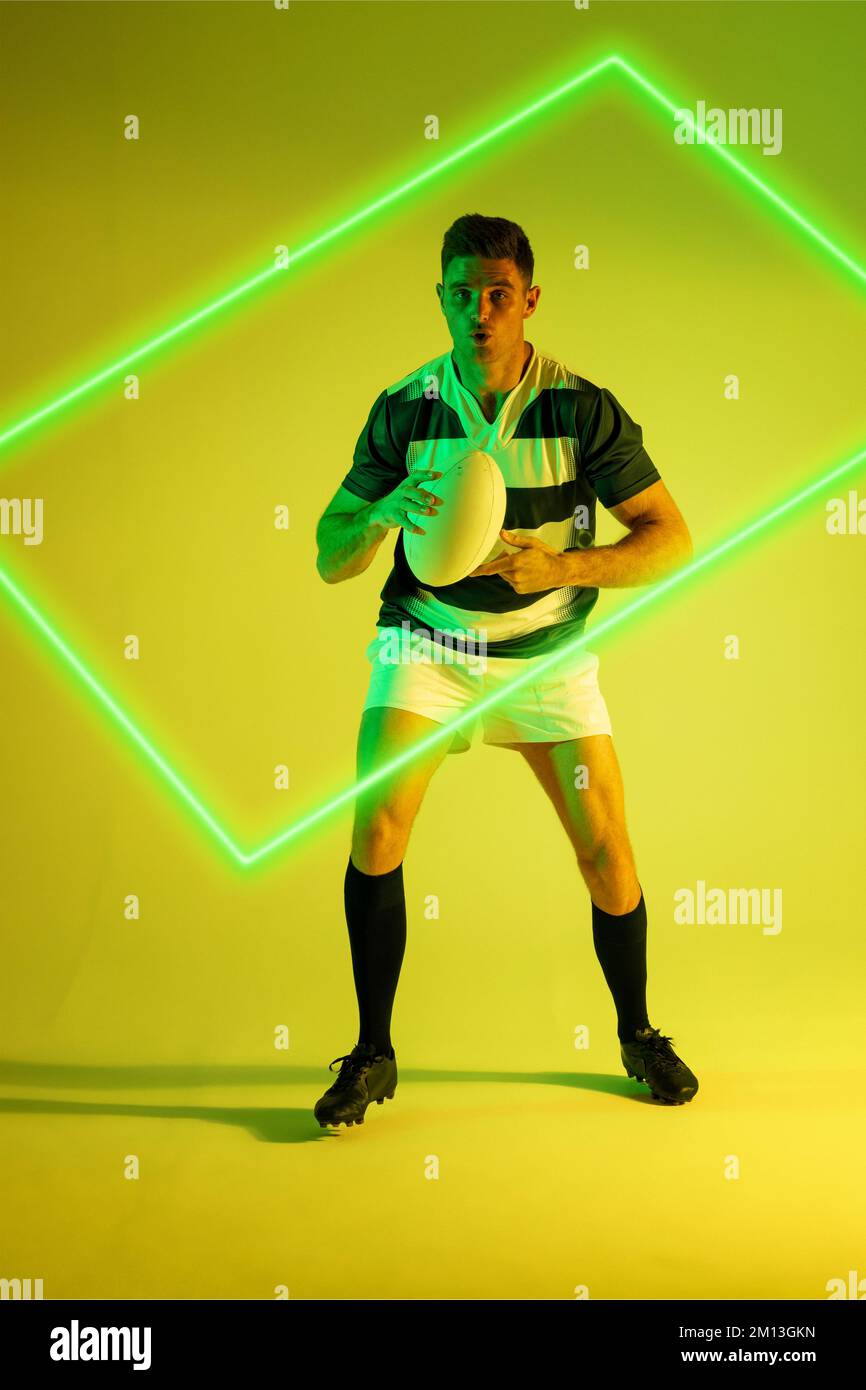 Tutta la lunghezza del giocatore di rugby maschio caucasico con palla da rettangolo illuminato su sfondo colorato Foto Stock