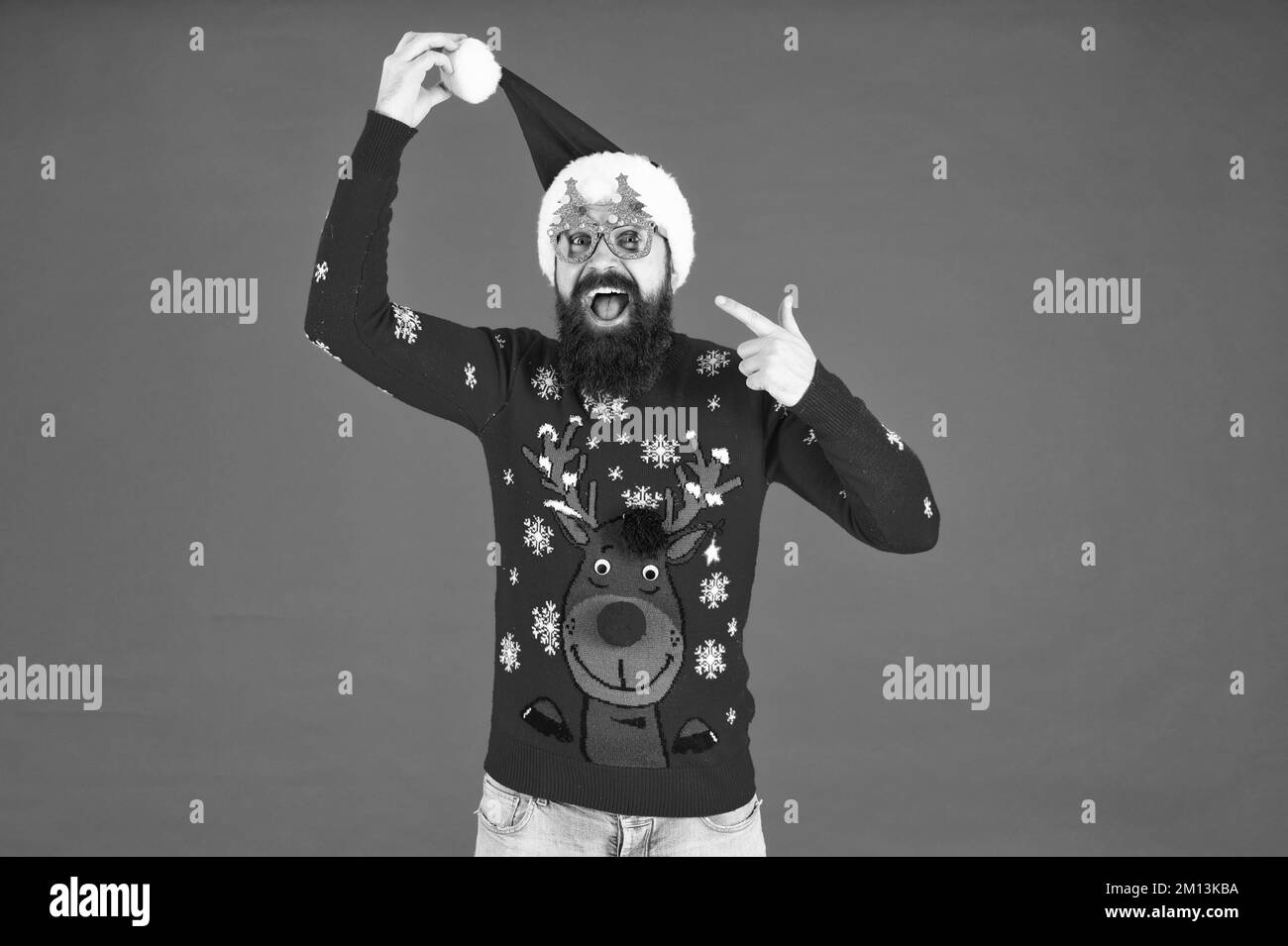 stupito uomo barbuto in cappello babbo natale puntando dito su occhiali da festa su sfondo rosso, babbo natale Foto Stock