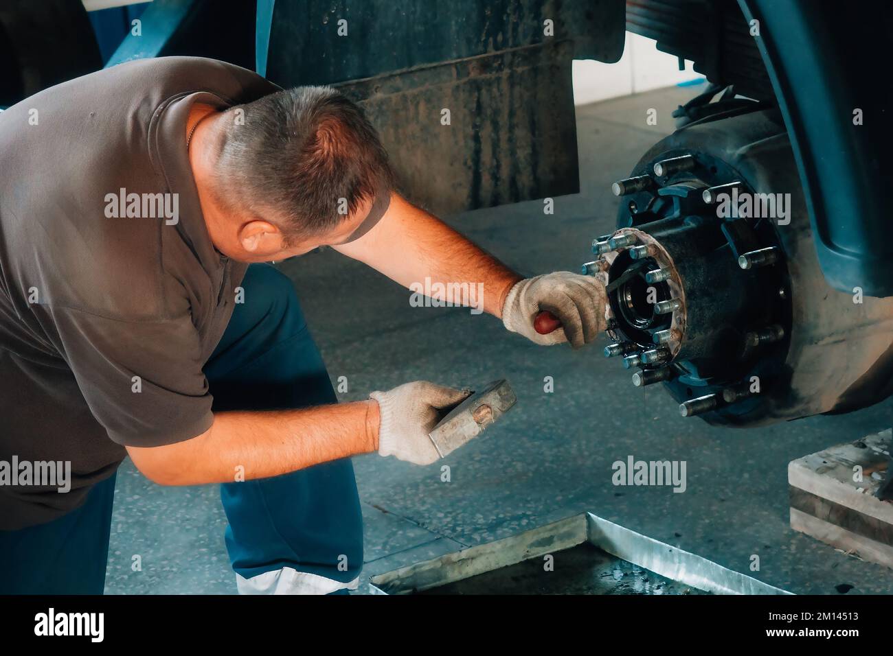 Meccanico auto ripara mozzo di camion in officina di riparazione auto. L'uomo caucasico bianco in guanti dismonta l'auto. Assistenza per la riparazione di carrelli e trattori di grandi dimensioni. Sfondo. Flusso di lavoro reale... Foto Stock