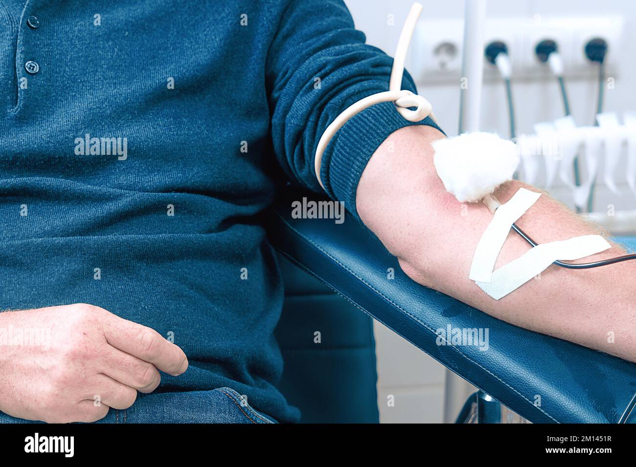 Tema della donazione. L'uomo dona sangue in ospedale. La mano della persona con l'ago e IV. Primo piano. Il donatore si siede sulla sedia. Sfondo.. Foto Stock
