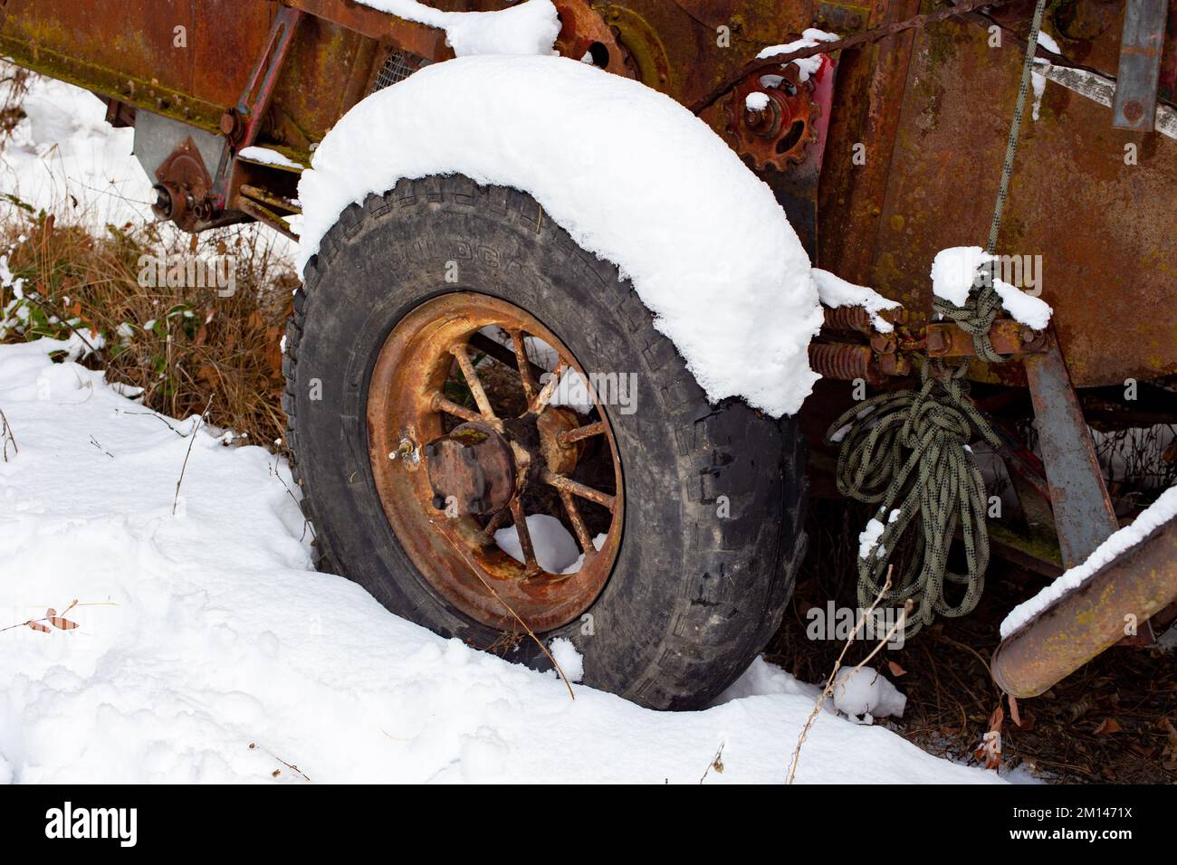 La ruota di acciaio a raggi su una arrugginita McCormick-Deering No.63 Harvester Thresher nella neve, sul bordo dei boschi, al di fuori di Bonners Ferry, Idaho. Foto Stock
