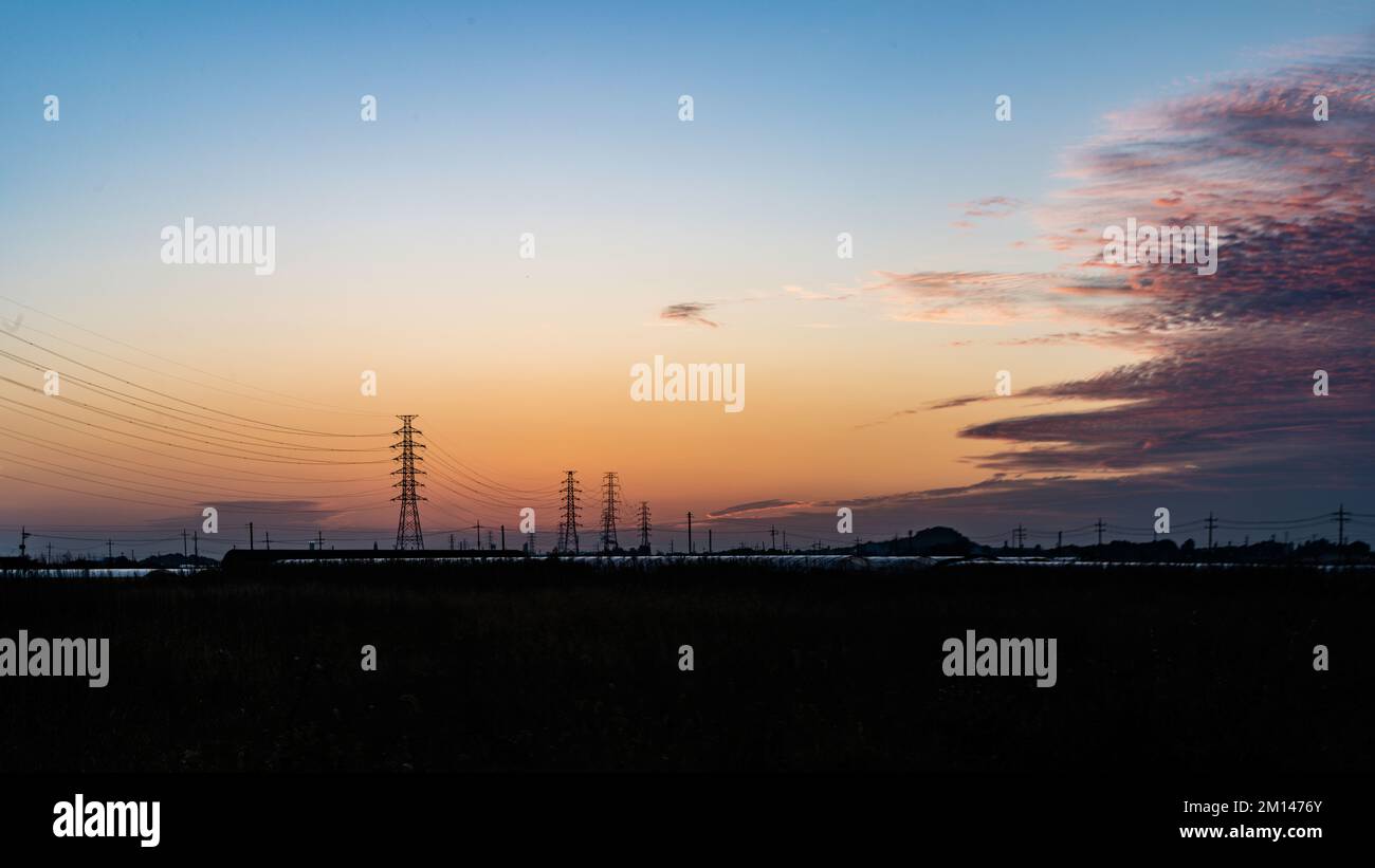 Una spettacolare fotografia al tramonto su una vasta pianura rurale con linee elettriche e pali di servizio che si ritirano nell'orizzonte lontano al crepuscolo Foto Stock