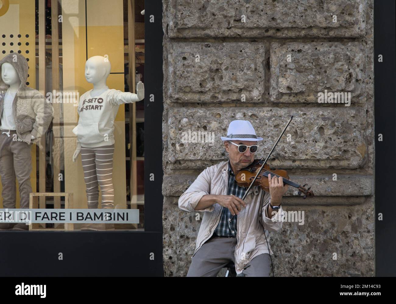 Un violinista suona all'esterno di una finestra di visualizzazione del negozio. Foto Stock