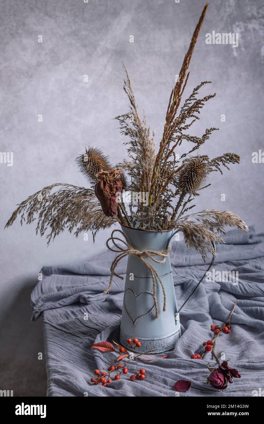 Piante e fiori secchi in vaso d'annata con un piccolo cuore su un tavolo con una sciarpa Foto Stock