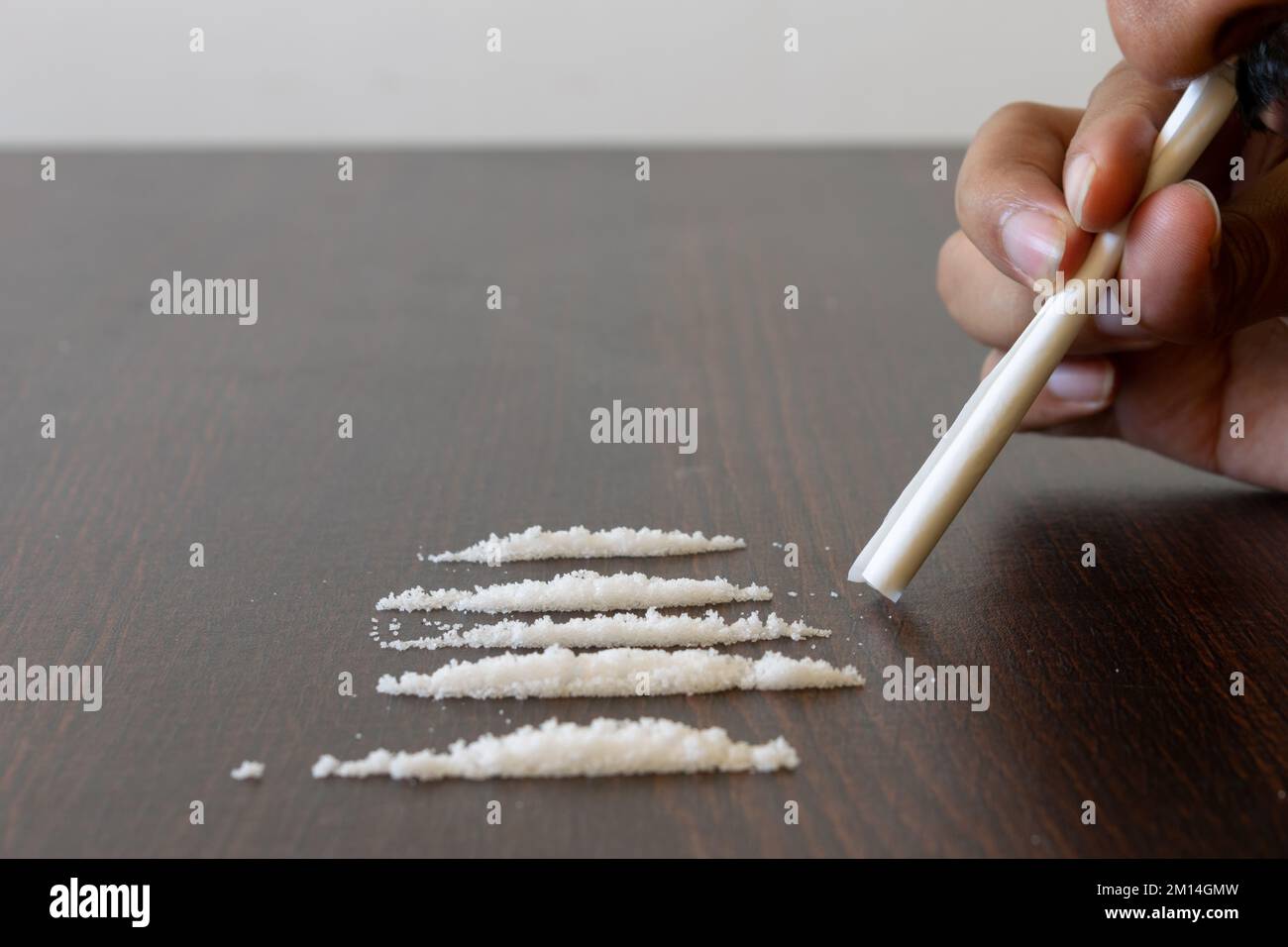 Immagine della mano del tossicodipendente che tiene carta avvolta insieme a righe di stupefacenti (cocaina ed eroina) Foto Stock