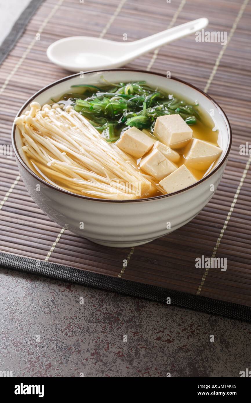 Zuppa giapponese vegetariana di shiro miso con tofu, funghi enoki, alghe wakame primo piano in una ciotola sul tavolo. Verticale Foto Stock