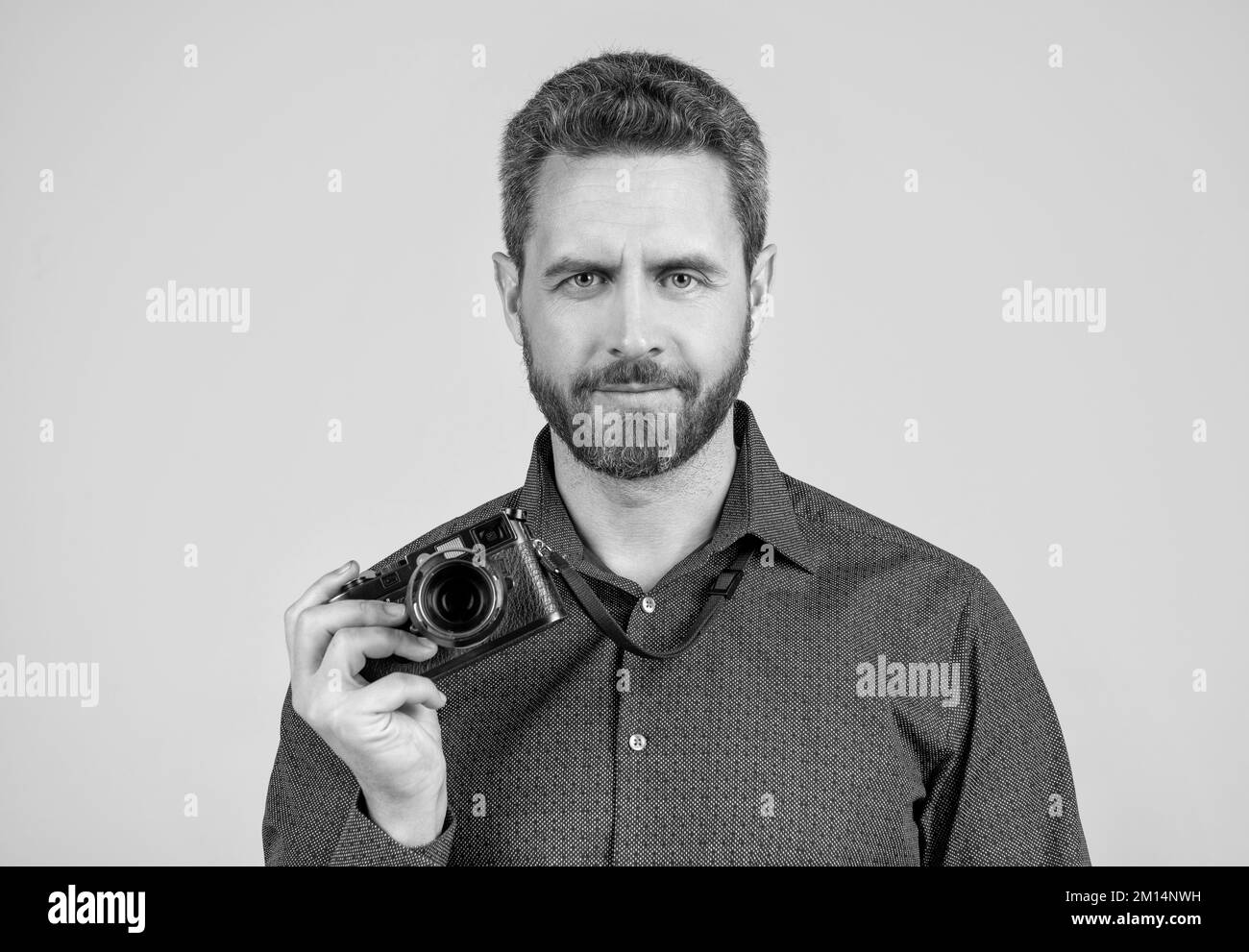 Uomo bearded in stile casual tenere fotocamera compatta sfondo grigio, cameraman Foto Stock