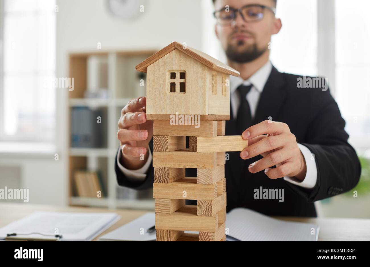 Man rimuove i blocchi dal modello di casa come concetto di mercato immobiliare instabile e rischi aziendali Foto Stock