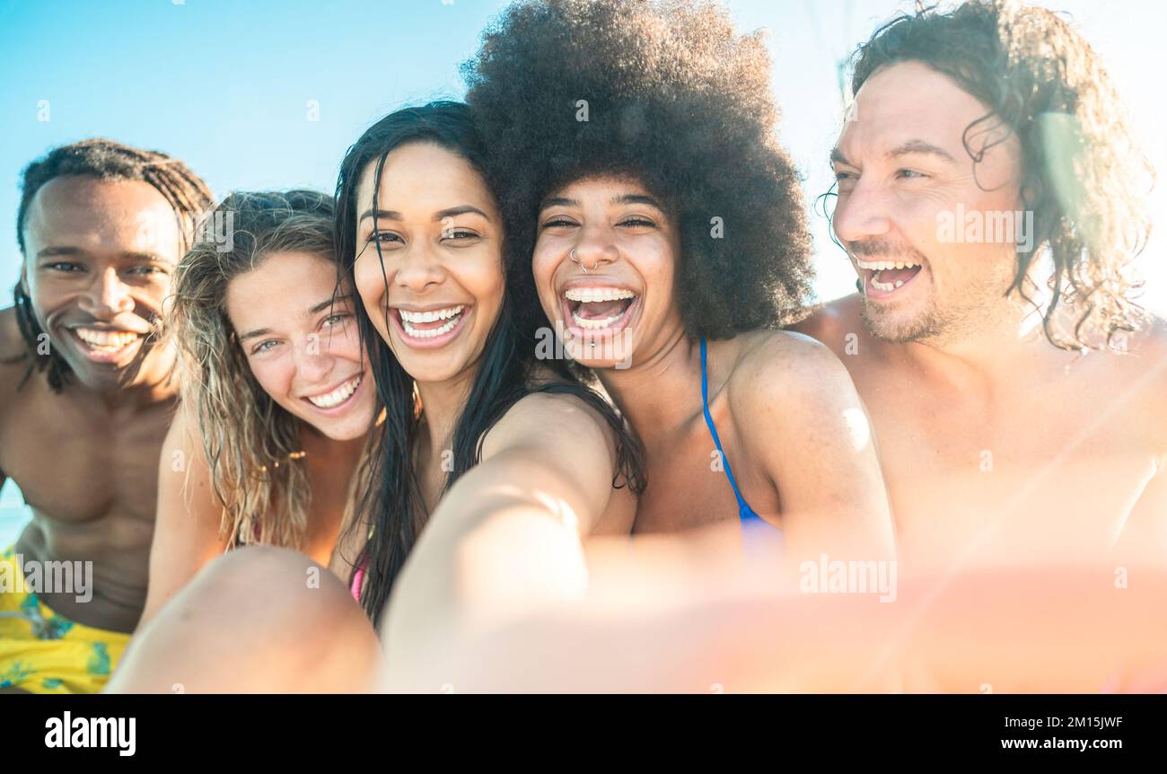 Bella giovane donna brasiliana sorridente e prendendo selfie guardando la fotocamera insieme i suoi amici - multirazziale gruppo di amici rilassarsi sul bea Foto Stock