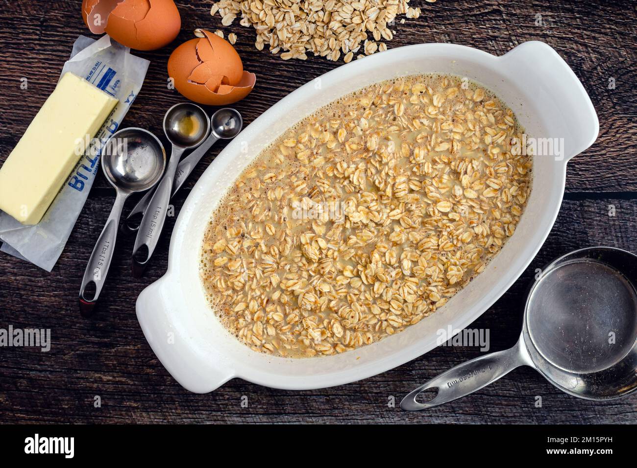 Avena arrotolata, latte e altri ingredienti di farina d'avena cotta al forno in un piatto da forno ovale: Farina d'avena cruda vista dall'alto e circondata da ingredienti Foto Stock