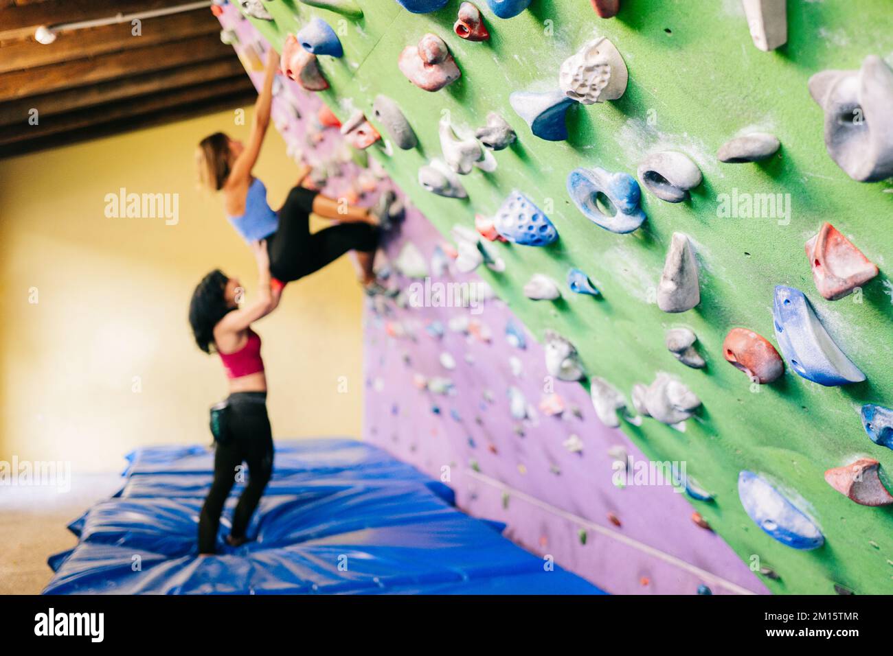 Allenatore femminile che sostiene l'arrampicatore sul muro durante l'allenamento di bouldering in palestra durante il giorno Foto Stock