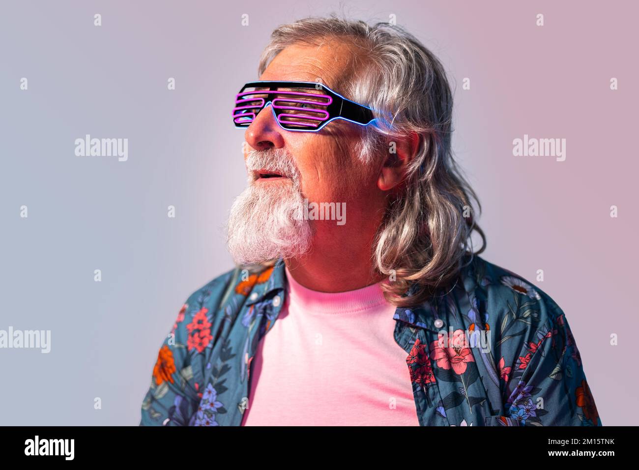 Uomo anziano barbuto in occhiali da sole rave al neon incandescente  guardando lontano su sfondo rosa Foto stock - Alamy