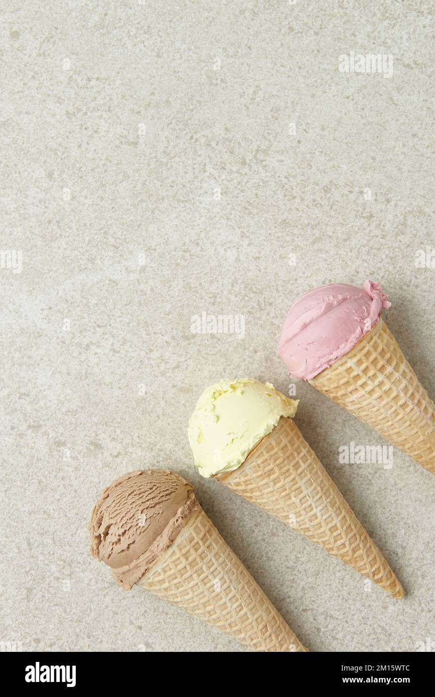 Vista dall'alto di appetitosi cioccolatini alla vaniglia e gelati alle bacche in croccanti coni di waffle disposti in fila su una superficie di marmo Foto Stock