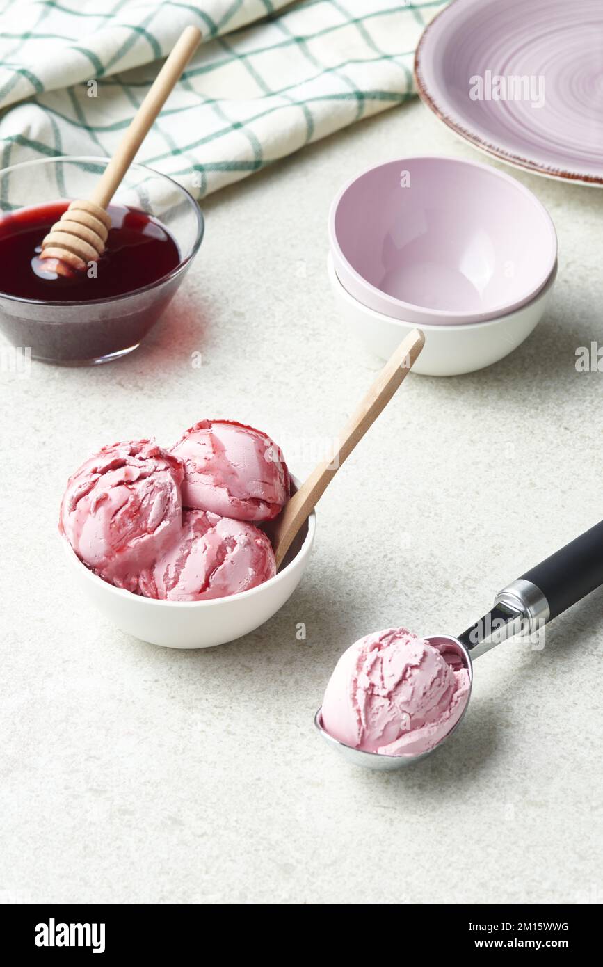 Angolo alto di cucchiai di deliziosi gelati fatti in casa serviti in un recipiente e ricoperti di sciroppo di bacche in una cucina leggera Foto Stock