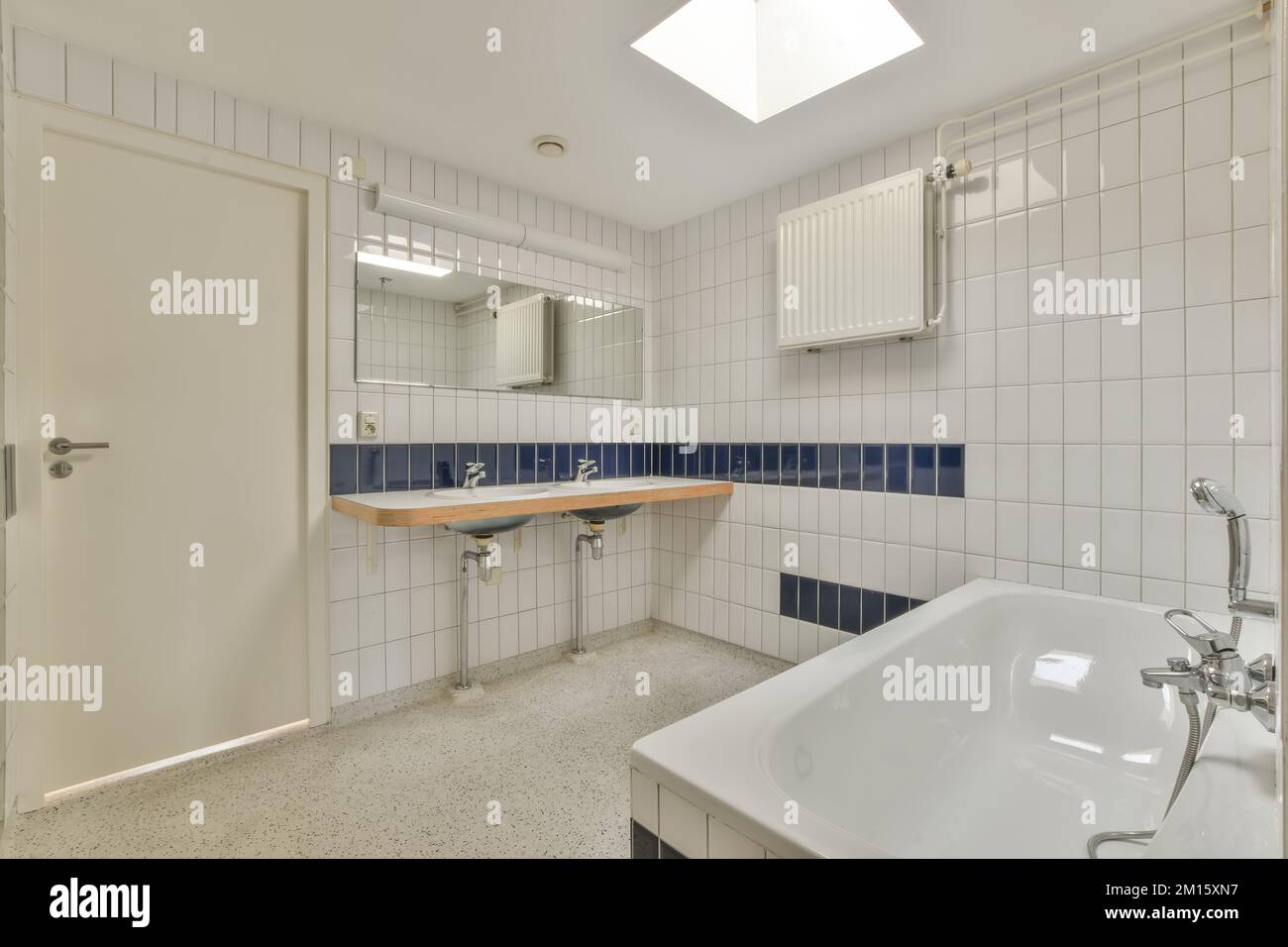 Interno di ampio bagno con doppio lavabo in ceramica e rubinetti cromati e specchio appeso su una parete piastrellata Foto Stock