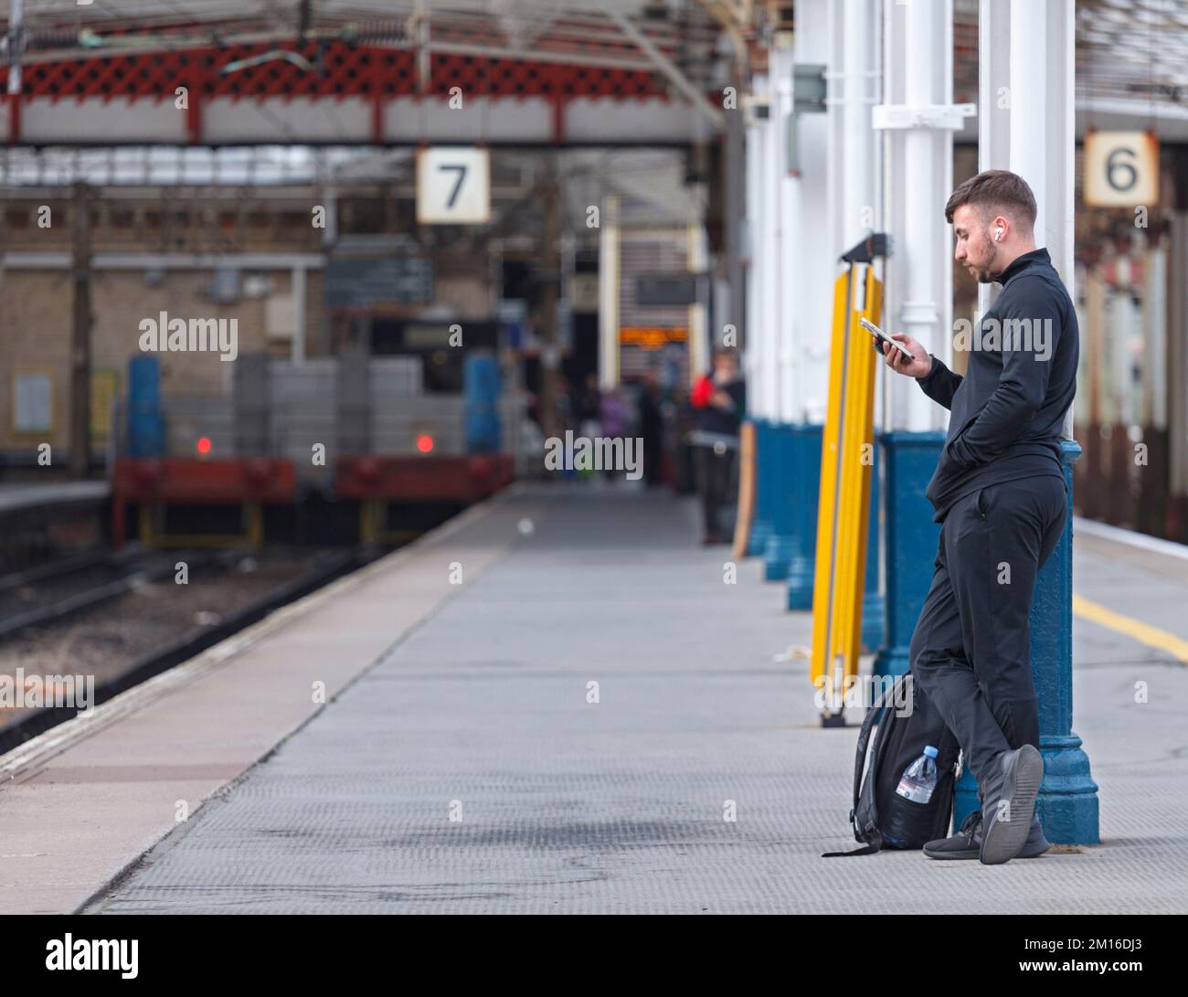 Passeggero ferroviario che guarda il suo telefono su una piattaforma deserta stazione ferroviaria a Crewe, Regno Unito Foto Stock