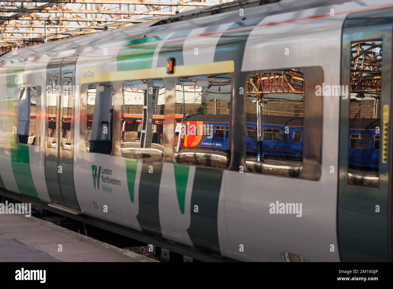 Treno di classe 156 della East Midlands Railway riflesso nella finestra di un treno di classe 350 della West Midlands alla stazione ferroviaria di Crewe, Regno Unito Foto Stock