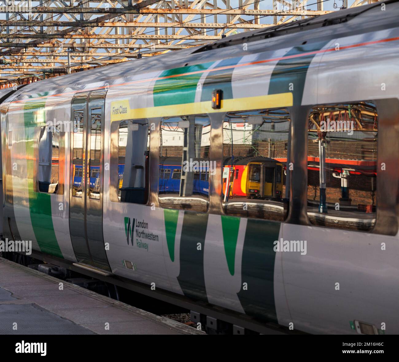 Treno di classe 156 della East Midlands Railway riflesso nella finestra di un treno di classe 350 della West Midlands alla stazione ferroviaria di Crewe, Regno Unito Foto Stock