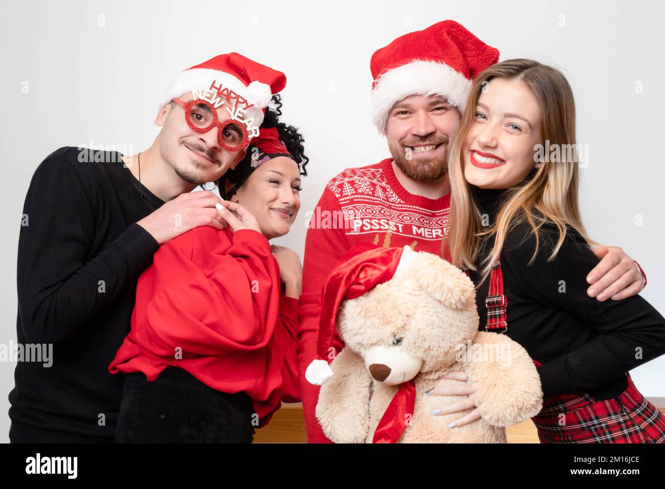 Quattro amici che festeggiano il nuovo anno, con un aspetto felice e allegro con occhiali prop e orsacchiotto Foto Stock