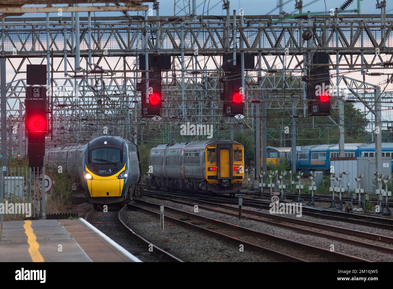 Avanti West Coast Pendolino treno e trasporto per lo sprinter Wales passando al bivio di Crewe sud con segnali rossi su un portale Foto Stock