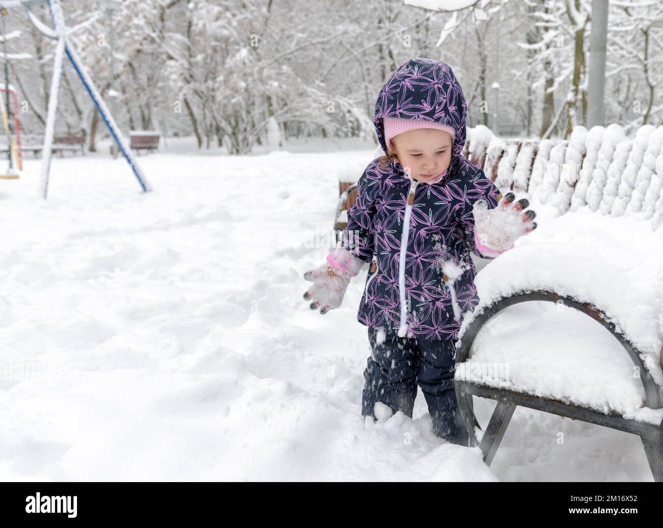 I bambini giocano con la neve in inverno, i bambini piccoli camminano nel parco urbano innevato durante le nevicate. La bambina è sullo sfondo della neve. Tema di freddo, gelo, inverno, Foto Stock