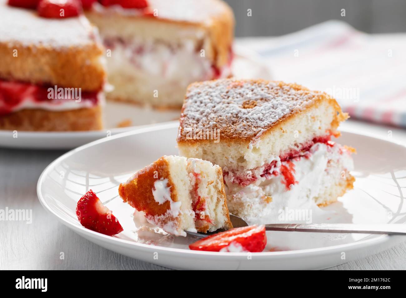Mangiare un pezzo di torta Victoria biscotto con panna montata, marmellata e fragole fresche. Foto Stock