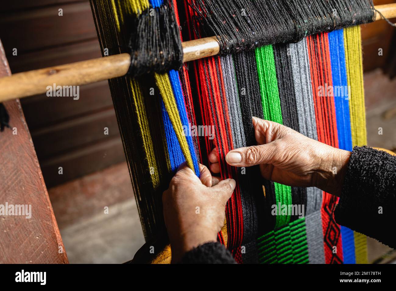 Mani di donna anziana irriconoscibile utilizzando un telaio artigianale fatto in casa per tessere lana colorata Foto Stock