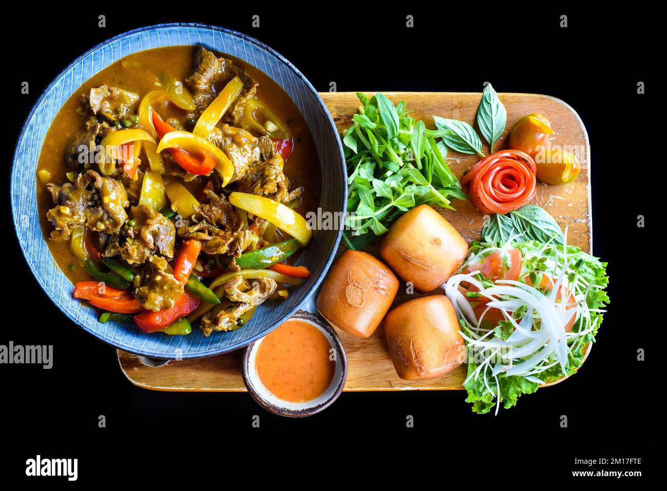 Stufato di manzo con verdure e pane mi banh su tagliere di legno isolato su sfondo nero Foto Stock