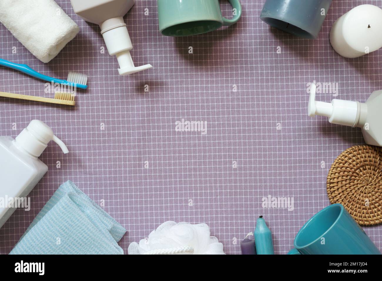 Bagno con prodotti per la doccia idromassaggio. spazzolino da denti, asciugamano, bottiglia di sapone per shampoo, tazza, candela sullo sfondo del tessuto viola a motivo di controllo. disposizione piatta, vista dall'alto, copia Foto Stock