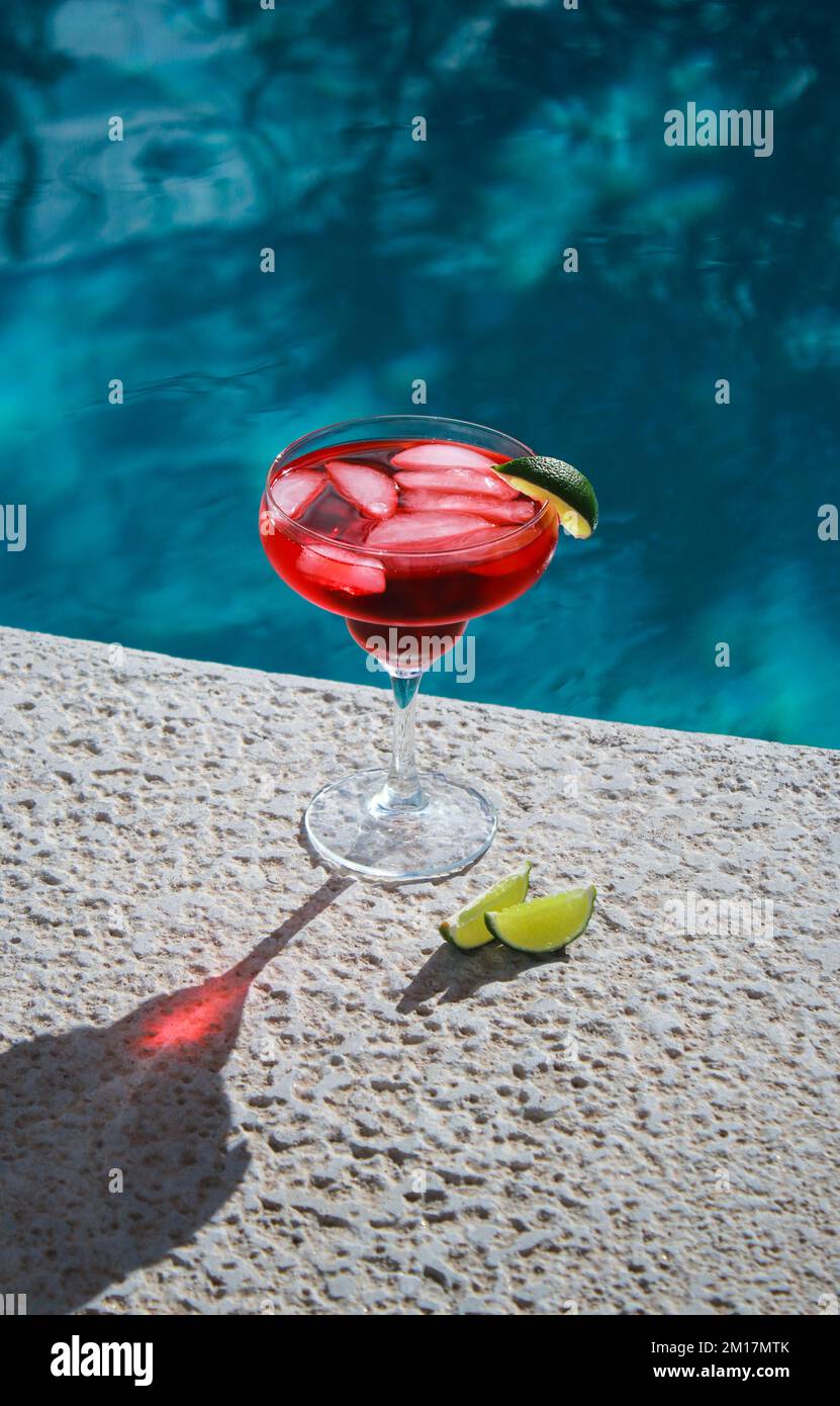 Primo piano di cocktail rosso rinfrescante con lime verdi in piscina Foto Stock