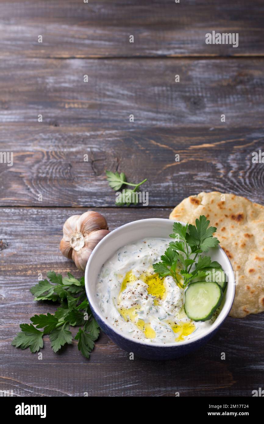 Tradizionale salsa tzatziki allo yogurt greco con cetrioli ed erbe su sfondo di legno, vista dall'alto, spazio Foto Stock