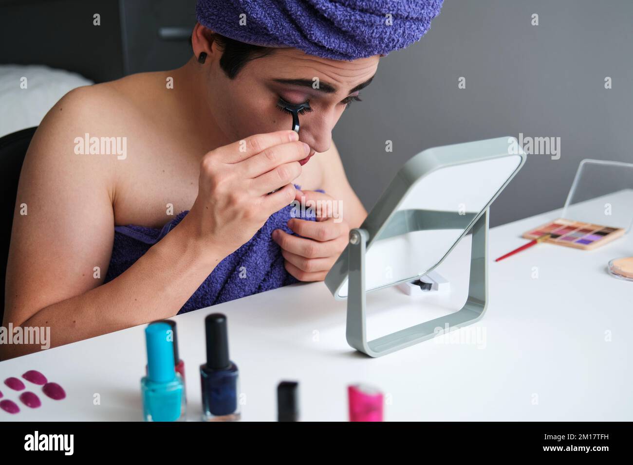 Giovane uomo transgender attaccante le ciglia false. Foto Stock